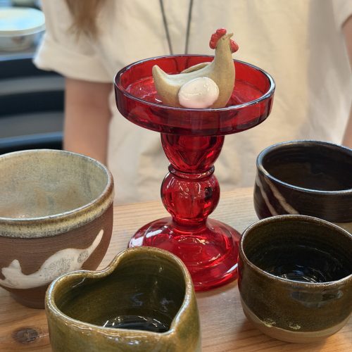 A close-up of ceramic cups and a ceramic chicken standing on a translucent red elevated platform at a booth in Central Market, Hong Kong, on April 10, 2026. Photo by Chen Meiyi.